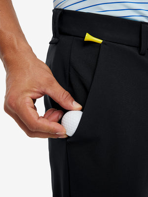 Hand placing a golf ball into pocket of water-resistant golf stretch nylon pants in black.