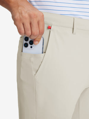 Hand placing an iPhone into pocket of soft lightweight casual golf pants with 5 pockets in cream.